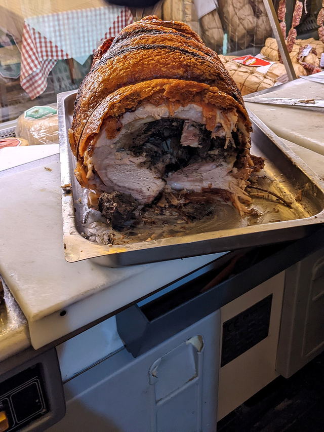 Una porchetta intera arrotolata e legata, appoggiata sul vassoio dentro la vetrina refrigerata, con il taglio già iniziato.