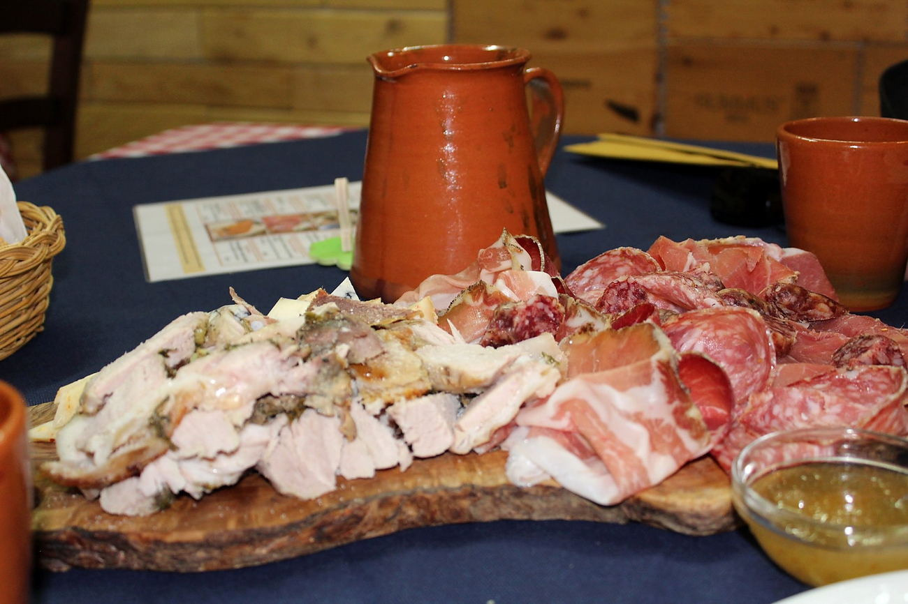 Il tagliere «Ci pensa Pippo» su un tagliere d'olivo: porchetta affettata, salumi e formaggi, con la brocca di terracotta e il pane sul tavolo blu.