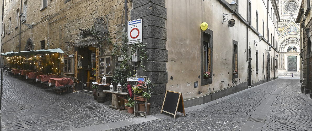 Il vicolo di Via Pedota: a sinistra i tavoli all'aperto della bottega sotto la tenda, in fondo a destra la facciata del Duomo di Orvieto.